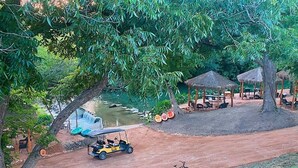 Ein Uferbereich mit einem pavilIon mit Strohdach, einem kleinen Bootssteg und einem Feldweg.