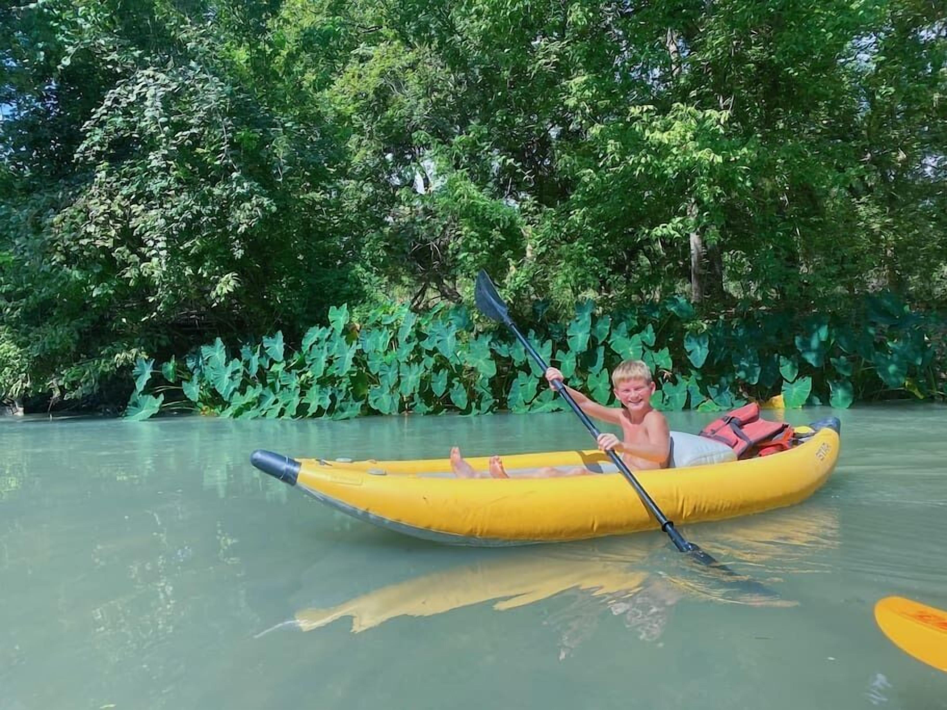 A person in a yellow inflatable raft on a calm river surrounded by lush greenery.