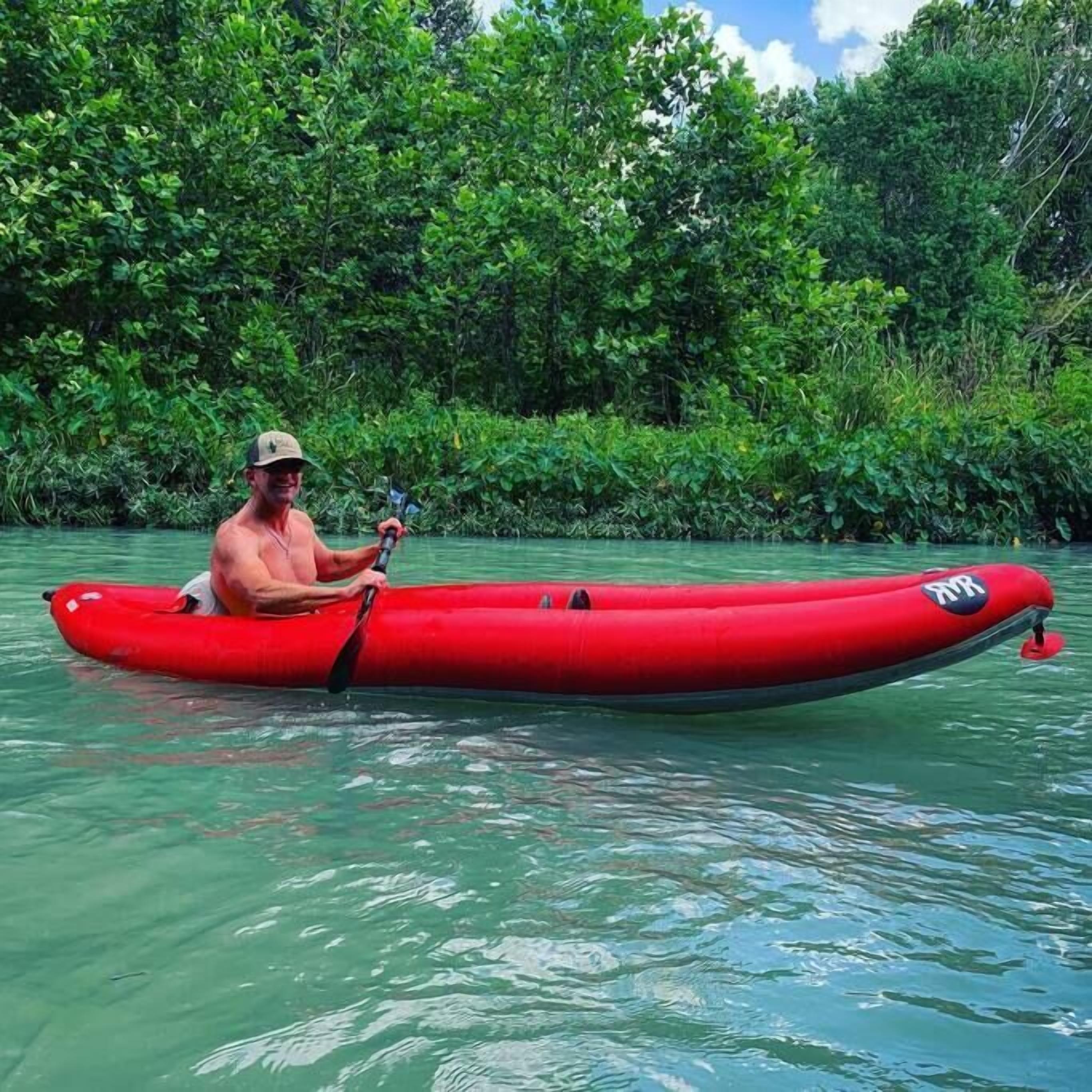 A man in a red kayak on a river surrounded by dense greenery.