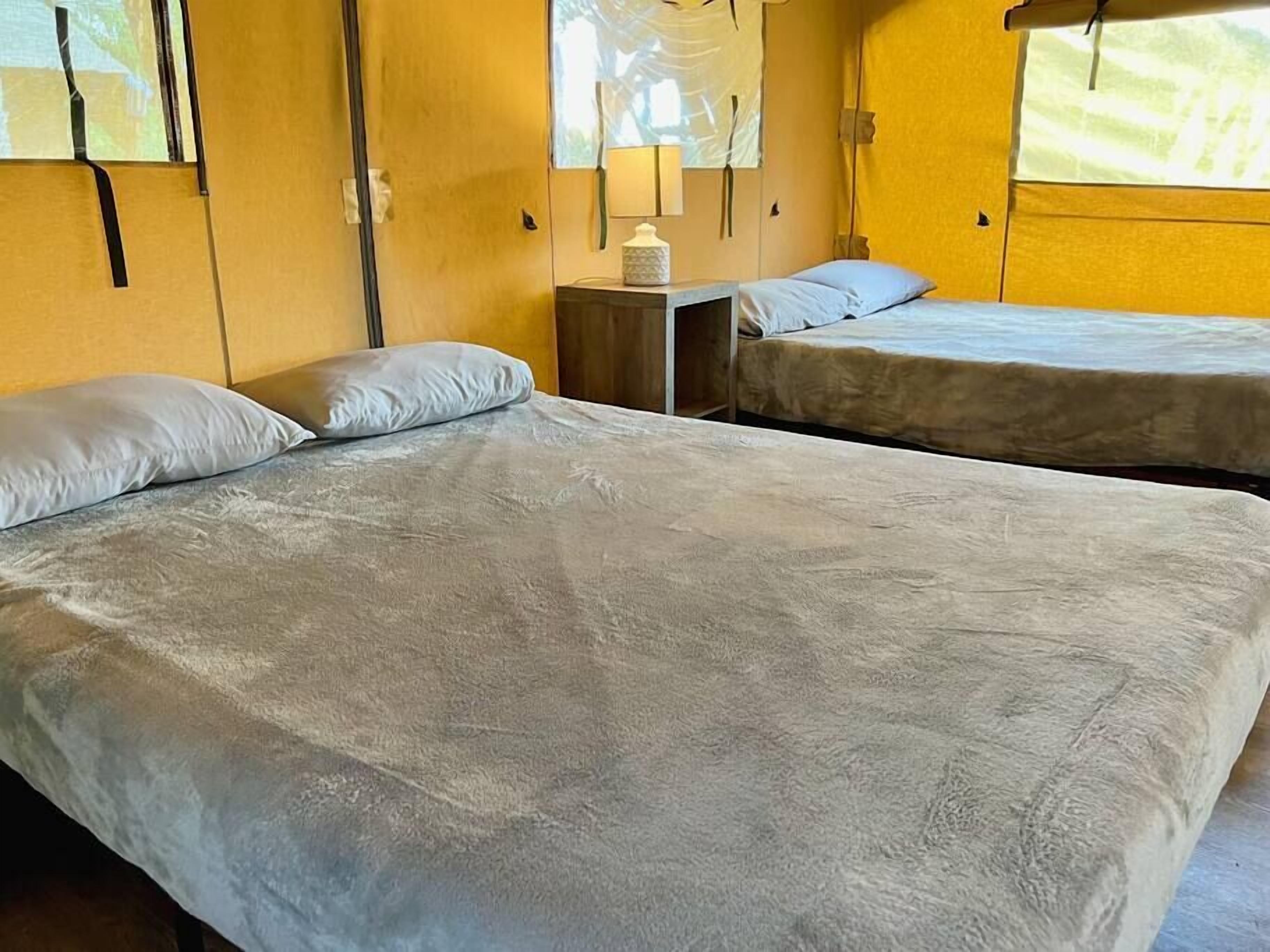 Ein Zimmer mit zwei Betten, einem kleinen Tisch mit Lampe und einem Fenster mit Blick.