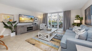 Uma sala de estar moderna com um sofá cinza, uma mesa de centro, uma televisão e uma varanda com cortinas.