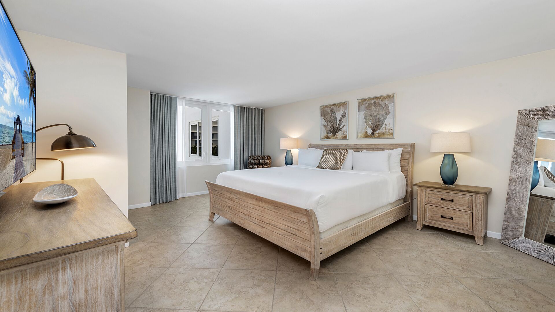 A hotel room with a large bed, bedside tables, a desk, a chair, a TV, and artwork on the walls.