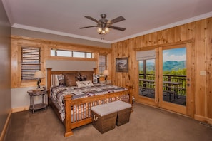 A bedroom with a wooden floor, a bed with a headboard, a ceiling fan, and a view of a balcony with outdoor seating. - Splashing at the Bluffs (Sevierville)