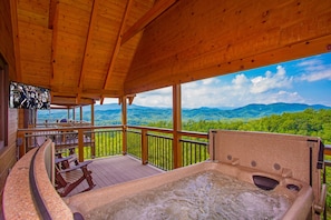 A wooden deck with a hot tub, wooden chairs, and a TV screen. - Splashing at the Bluffs (Sevierville)