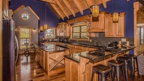 Une cuisine spacieuse avec des meubles en bois, un grand îlot central et un plafond haut avec des poutres apparentes.