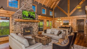 L’intérieur d’une cabane en rondins, avec une cheminée en pierre, des poutres en bois, un canapé et un coin repas.