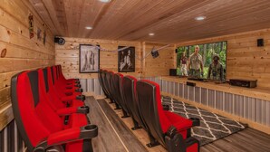Une rangée de chaises rouges et noires est placée face à un écran de télévision. Les murs et le plafond sont en bois.