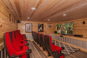 Une rangée de chaises rouges et noires est placée face à un écran de télévision. Les murs et le plafond sont en bois.