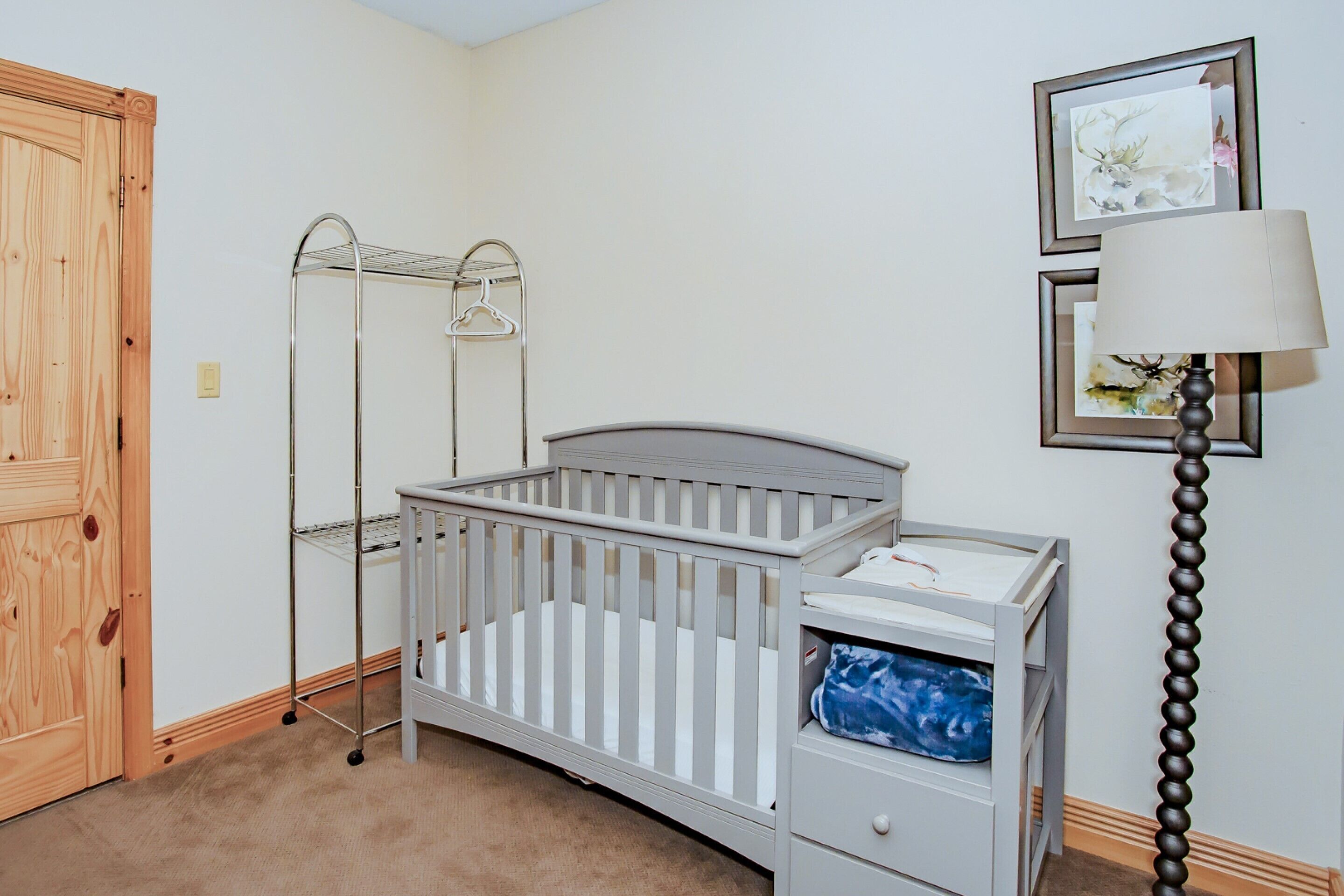 A baby crib with a changing table, a metal drying rack, and a lamp.