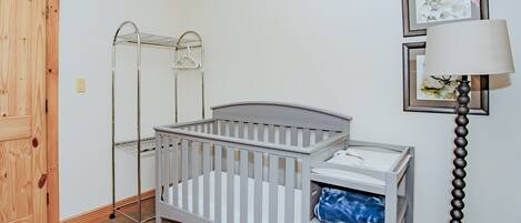 A baby crib with a changing table, a metal drying rack, and a lamp.