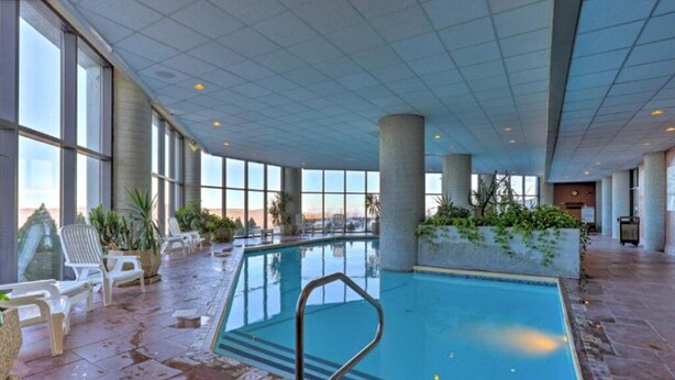 Una piscina interior con paredes de vidrio transparente, sillas de descanso y plantas en macetas.