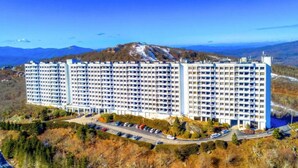 Un hotel grande de varios pisos con un patio central, rodeado por un área boscosa y vistas a montañas distantes.