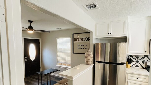 A modern kitchen with a stainless steel refrigerator, a dining area with a table and chairs, and a living room with a sofa. - Cute 2 bedroom in the heart of Houston  (Houston)