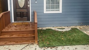 A house with a dark front door, a small window with blinds, a wooden staircase, and a front yard with grass and a gravel path. - Cute 2 bedroom in the heart of Houston  (Houston)
