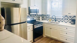 A modern kitchen with white cabinets, stainless steel appliances, a patterned backsplash, and a window with blinds. - Cute 2 bedroom in the heart of Houston  (Houston)