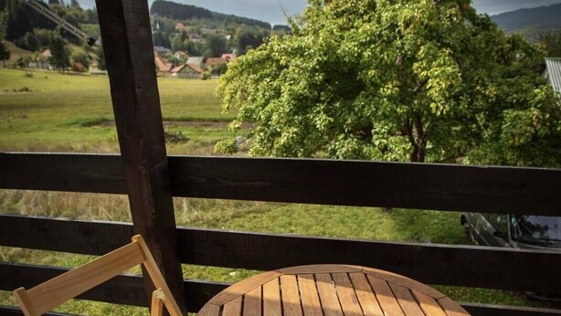 Mesa y silla de madera en un balcón con vistas a un árbol y un paisaje.