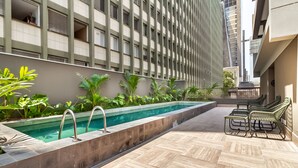 A rooftop pool area with a herringbone tile floor, surrounded by lush greenery and a seating area with metal chairs. - 360 Pamplona (São Paulo)