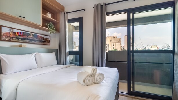 A hotel room with a large bed, a view of the city through a sliding glass door, and a painting on the wall. - 360 Pamplona (São Paulo)