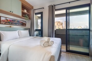 Habitación de hotel con una cama grande, vista de la ciudad a través de una puerta corrediza de vidrio y un cuadro en la pared.
