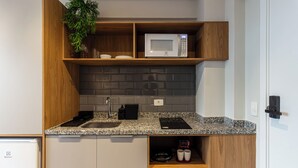 A modern kitchen with a granite countertop, built-in microwave, and wooden shelves. - 360 Pamplona (São Paulo)