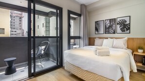 A modern hotel room with a large bed, a glass door leading to a balcony, and a view of the cityscape. - 360 Pamplona (São Paulo)