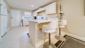 A modern kitchen with white cabinets, a central island with bar stools, and a small window.