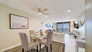 A dining area with a glass table and striped chairs, a ceiling fan, and a framed picture on the wall.