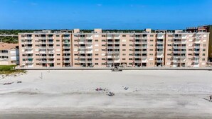 A multi-story residential building with balconies, located near a beach.