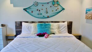 A neatly made bed with a quilted white duvet, a teal throw blanket, and a pink flower.