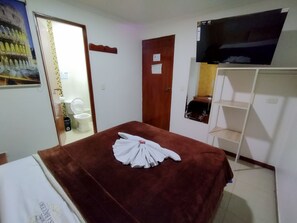 A hotel room with a bed, a television mounted on the wall, a wooden door, and a white wall with a framed picture.