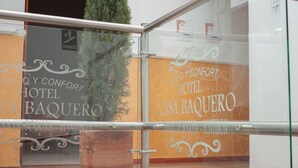 Een hotelentree met een glazen balustrade, een bloempot en decoratieve tekst aan de muur.