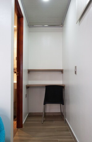 A narrow hallway with a wooden floor, a black chair, and a desk with shelves.