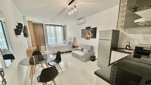A modern, well-lit living area with a dining table, chairs, a sofa, and a kitchen area with a refrigerator and sink. - COMODO MONOAMBIENTE EN EQUIPETROL CON PISCINA EN CONDOMINIO! (Santa Cruz de la Sierra)