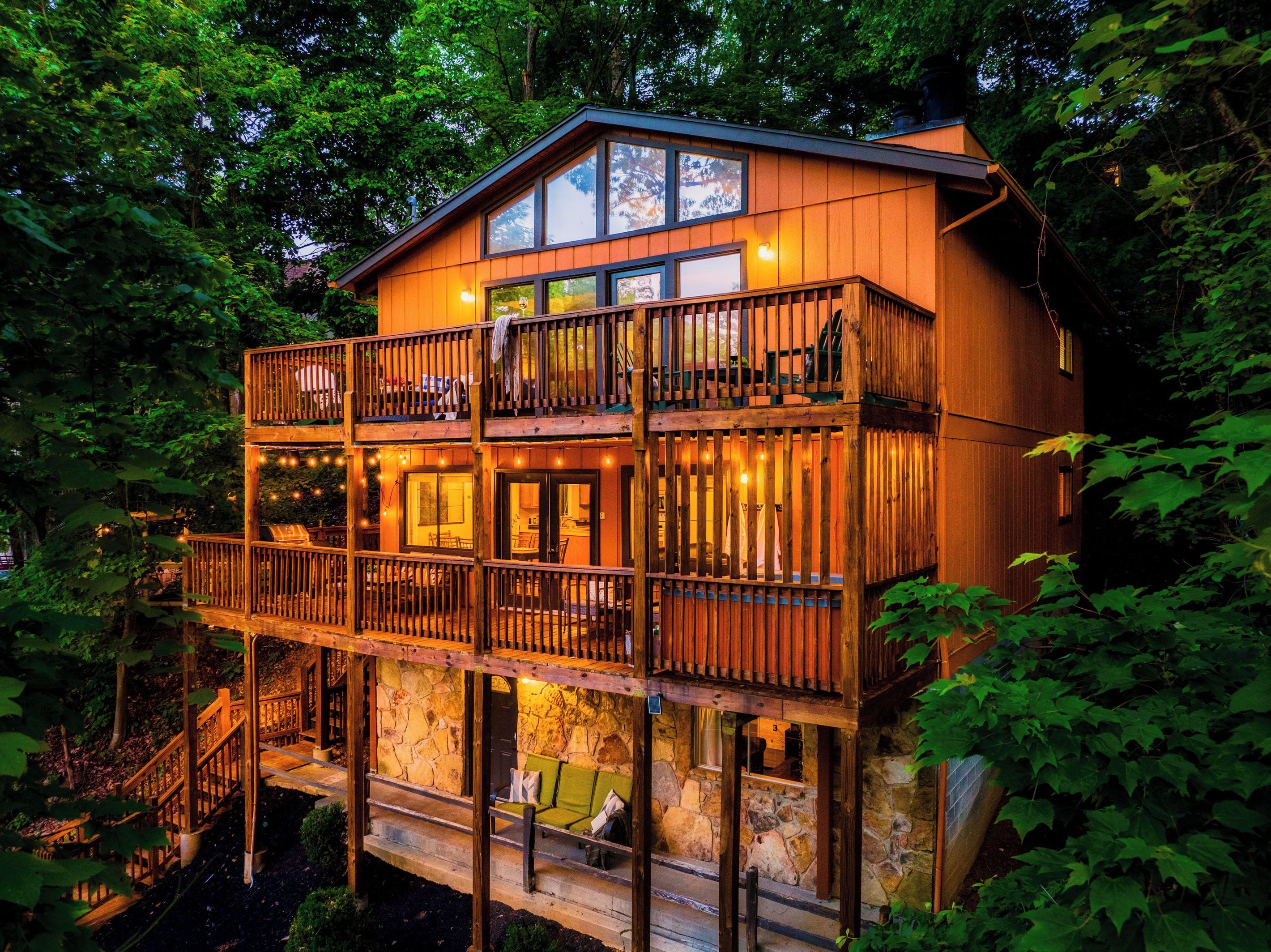 A two-story wooden cabin with a balcony, stone walls, and a staircase leading to the upper level.