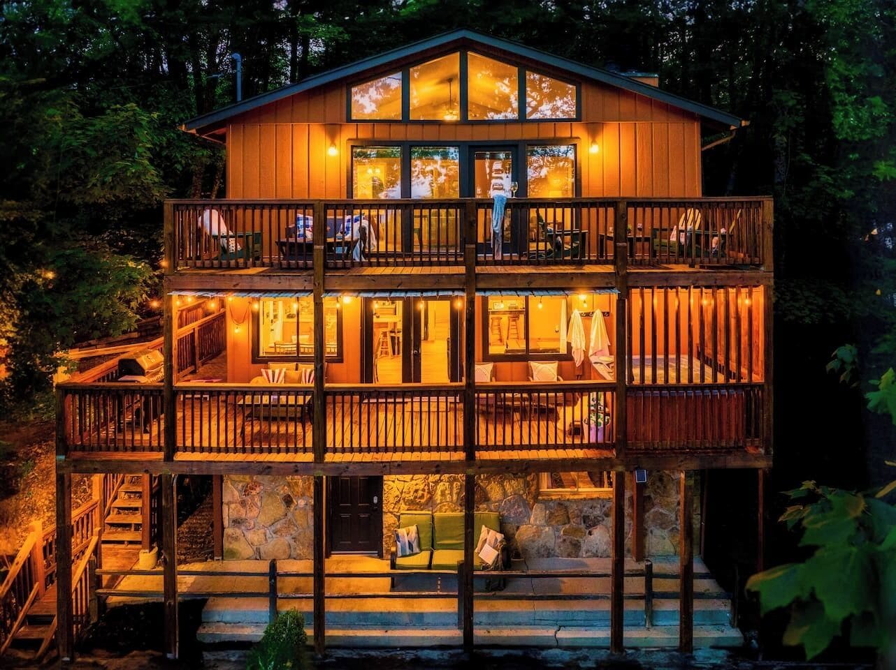 Eine mehrstöckige Holzhütte mit Balkonen, einem Steinfundament und warmer Innenbeleuchtung.