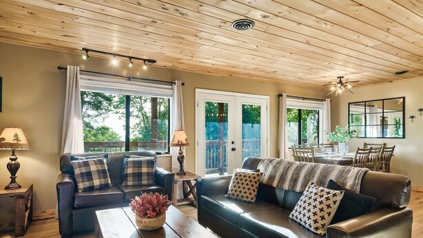 A cozy living room with a sofa, coffee table, and lamps. There is a dining area with a table and chairs visible through a glass door.