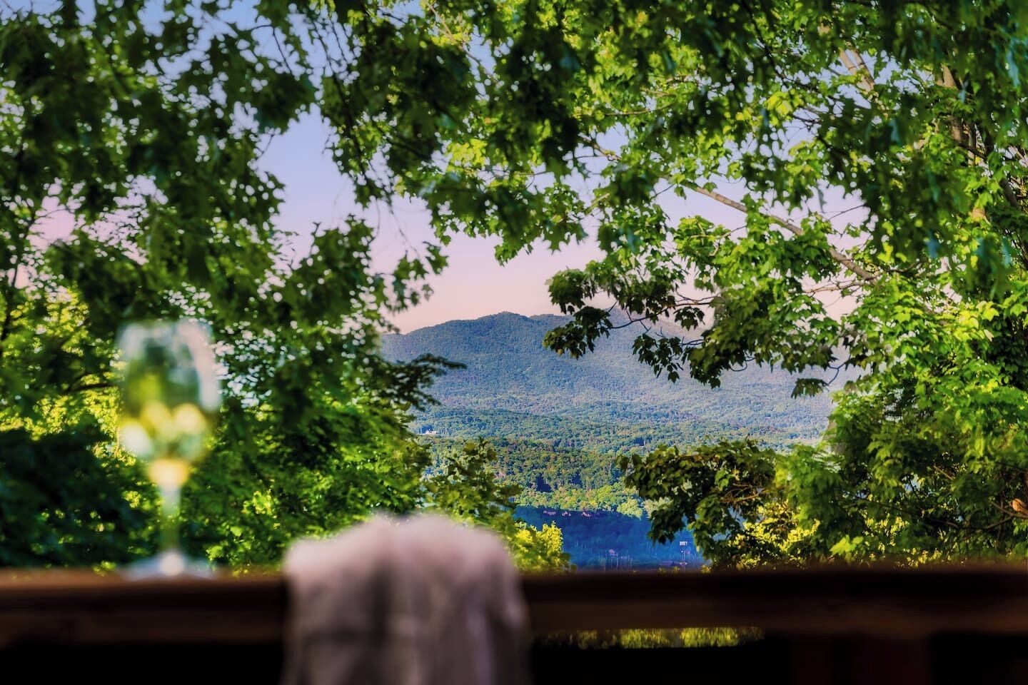 A view through a window with a wooden frame, a blurred foreground, and a landscape of a forested mountain range.