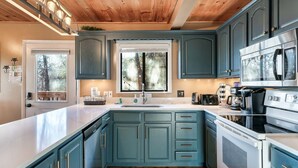 A kitchen with teal cabinets, a white countertop, a stainless steel oven, and a window with a view of trees.