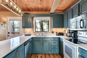 A kitchen with teal cabinets, a white countertop, a stainless steel oven, and a window with a view of trees.