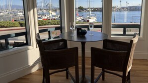 A dining area with a table and chairs, large windows with a marina view, and a glass of water on the table. - Luxury waterfront! The Pagoda Beach House (Oxnard)