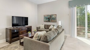 A modern living room with a flat-screen TV, a sofa, a coffee table, and a sliding glass door leading to an outdoor area.
