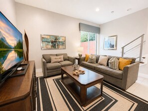 Sala de estar com sofá, mesa de centro e televisão. Há duas pinturas na parede.