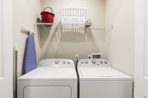 A laundry room with two front-loading washers and dryers, a red bucket, a white laundry basket, and a blue towel hanging on a rack.