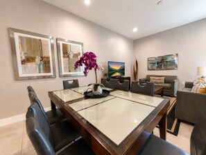 A modern living room with a glass-top dining table, a sofa, and a TV.