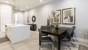 A modern kitchen with a central island, a dining area with a dark wooden table and black chairs, and a living space with a large mirror and artwork on the wall.