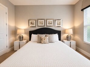 Une chambre à coucher avec un grand lit, deux tables de chevet, une tête de lit noire et quatre tableaux encadrés accrochés au mur.