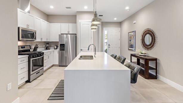 A modern kitchen with white cabinetry, stainless steel appliances, and a central island with a sink.