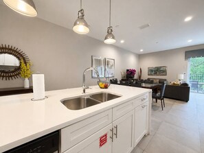 Une cuisine moderne avec un plan de travail blanc, un évier en acier inoxydable et des luminaires suspendus.