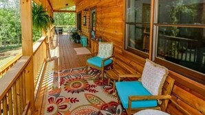 Eine hölzerne Veranda mit einem farbenfrohen Teppich, einer Bank und einem Sessel.