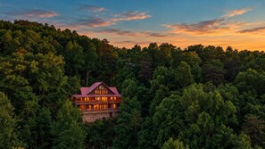 A large, multi-story lodge surrounded by dense forest, with a prominent red roof and multiple balconies.